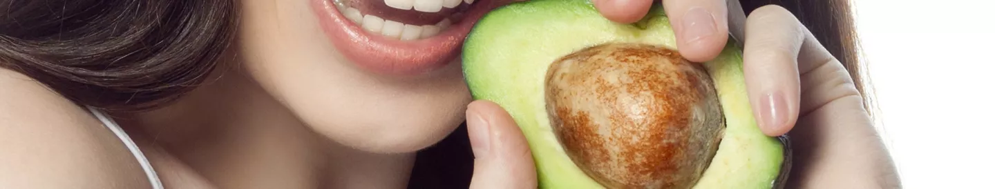 Mujer sonriendo mientras sostiene medio aguacate fresco con el hueso aún dentro, lista para pelarlo