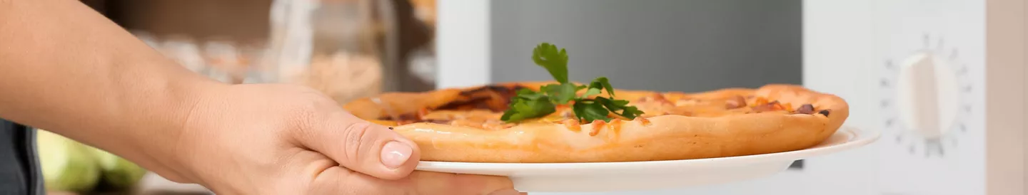 Persona sacando una pizza casera del microondas sobre un plato blanco, lista para servir