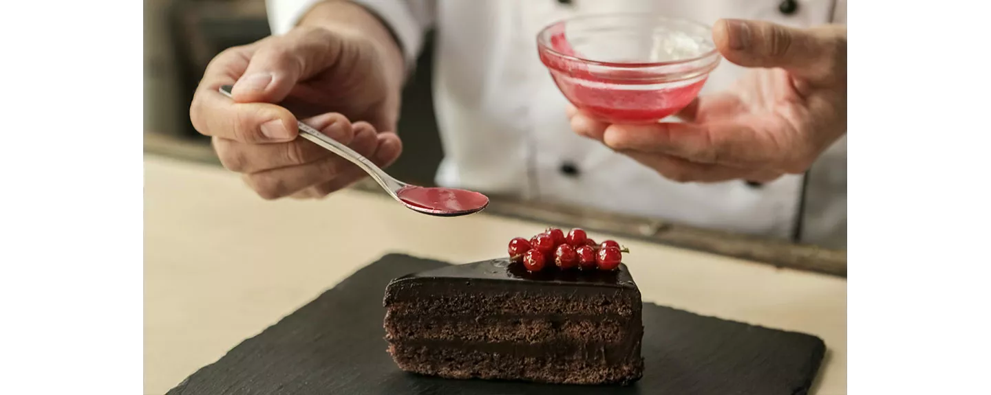 Un chef decorando un postres de pastel de chocolate con salsa de frutas rojas