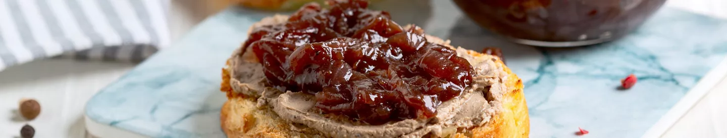Rebanada de pan tostado cubierta con paté y mermelada de cebolla caramelizada, presentada sobre una tabla de mármol.