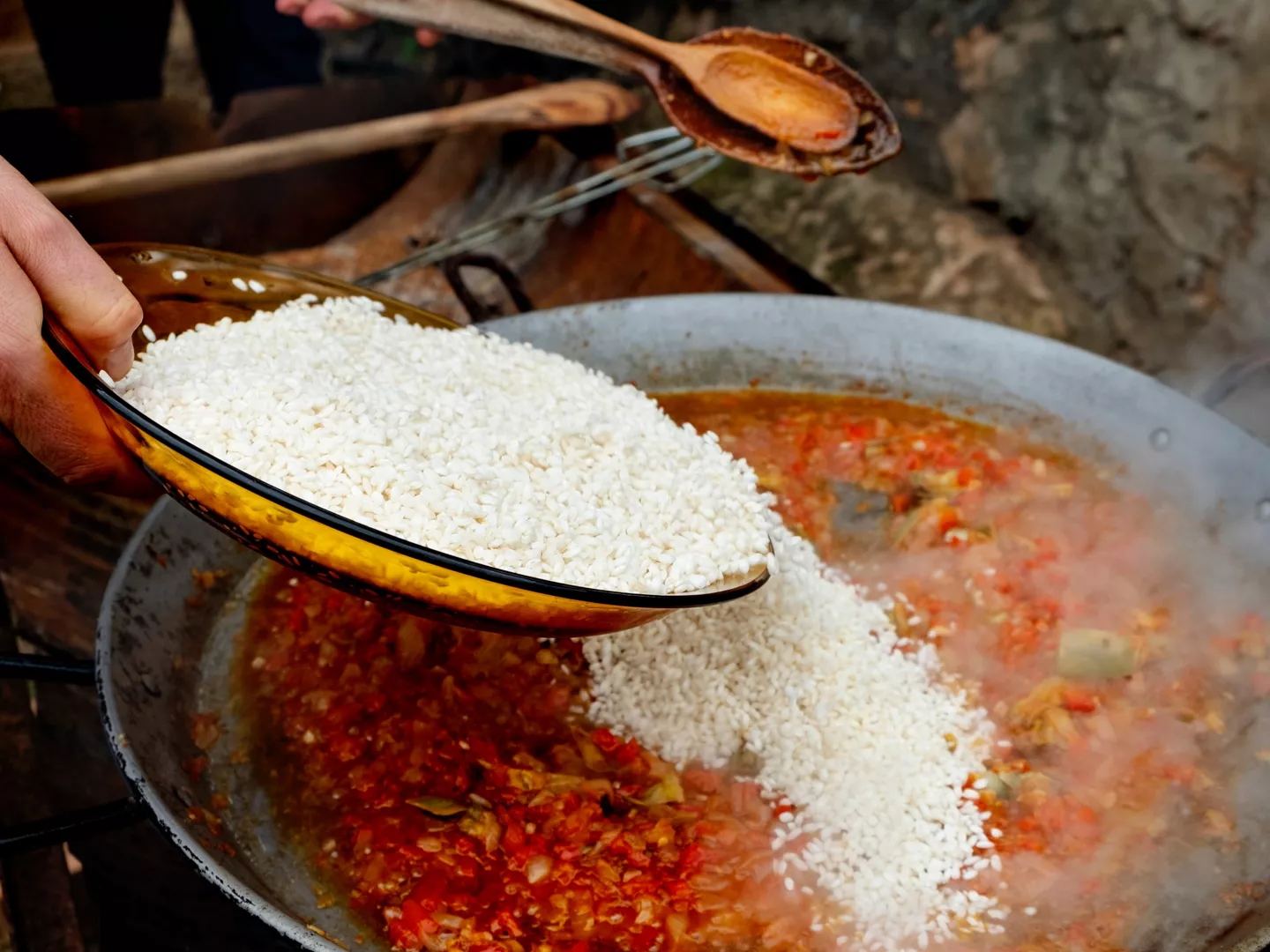 Añadiendo arroz bomba a la paellera con sofrito para preparar paella casera