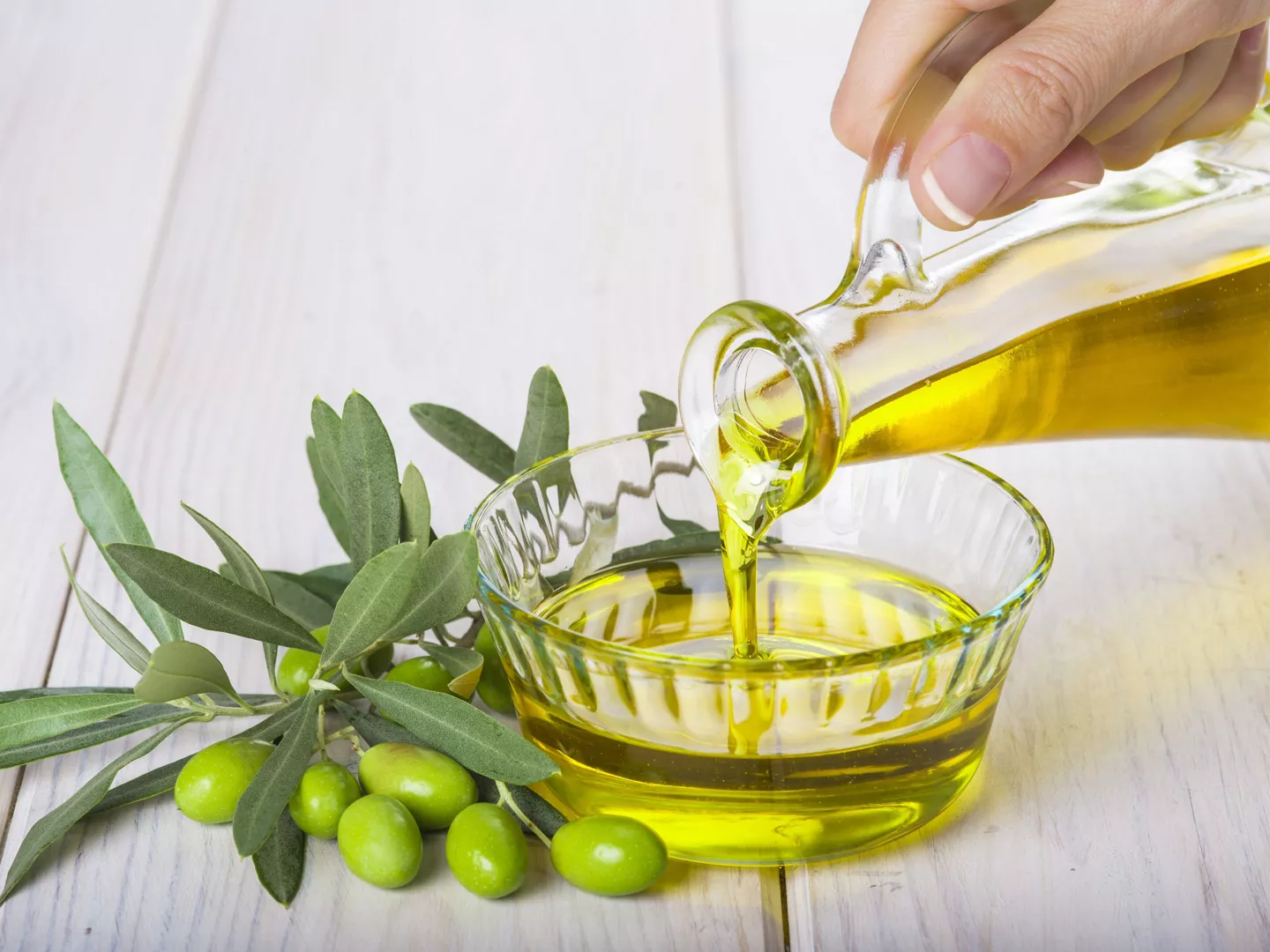 Mano vertiendo aceitera con aceite de oliva virgen en recipiente