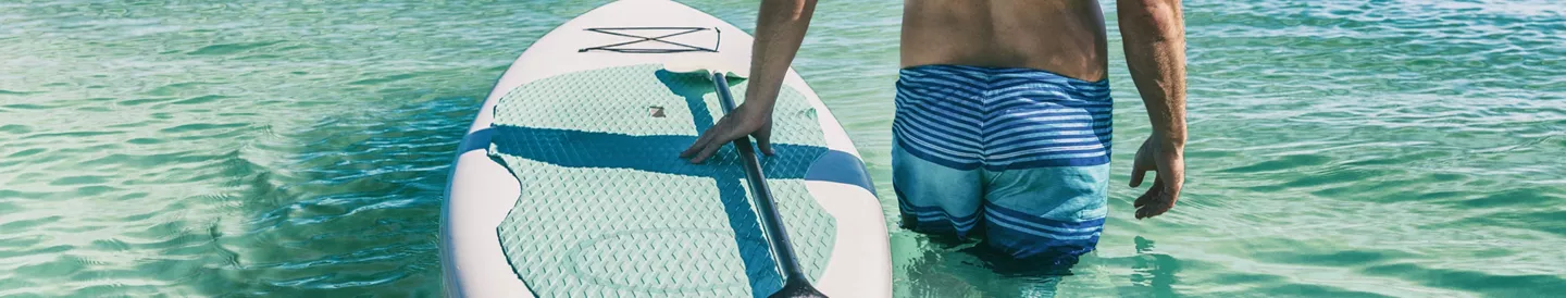 Hombre entrando al agua con tabla de paddle surf hinchable
