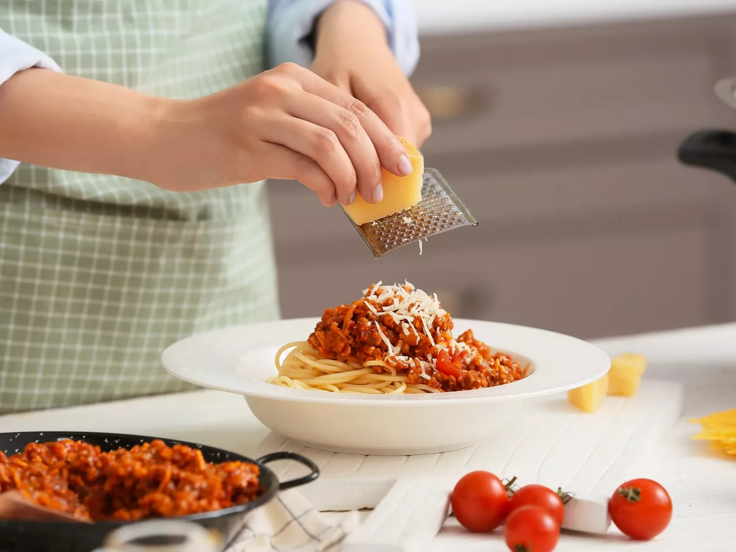Persona rallando parmesano sobre plato pasta salsa boloñesa