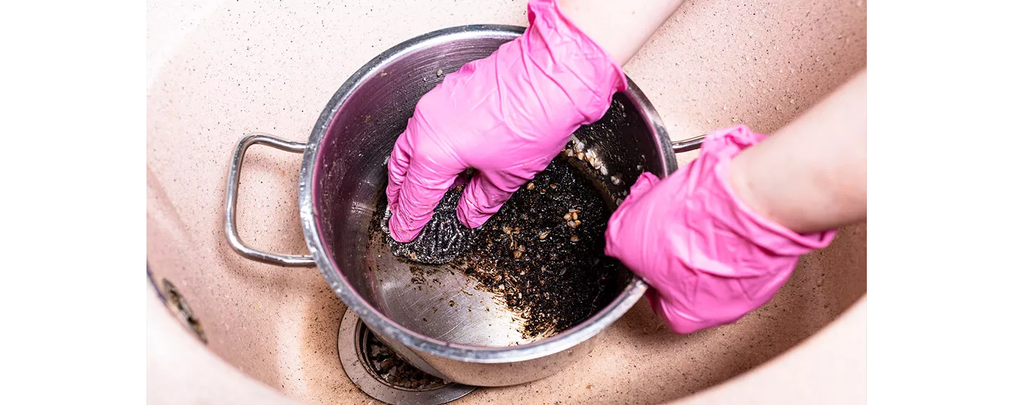 Una persona frotando el quemado de una olla con un estropajo