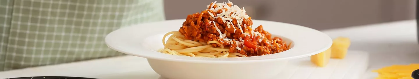 Persona rallando parmesano sobre plato pasta salsa boloñesa