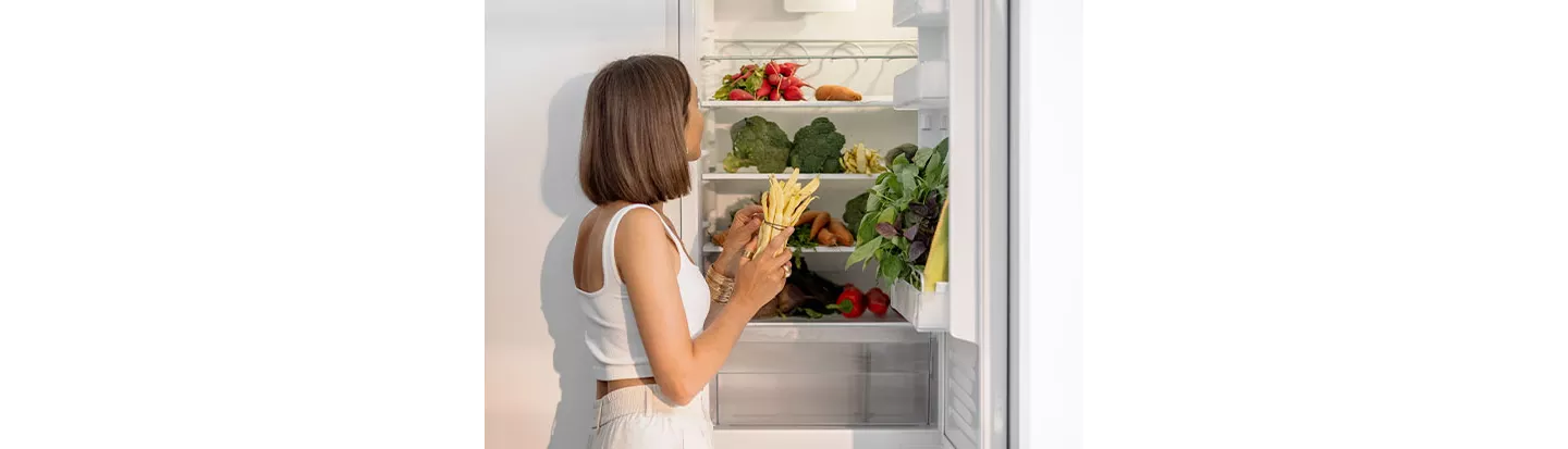Una mujer ordenando la nevera con verduras