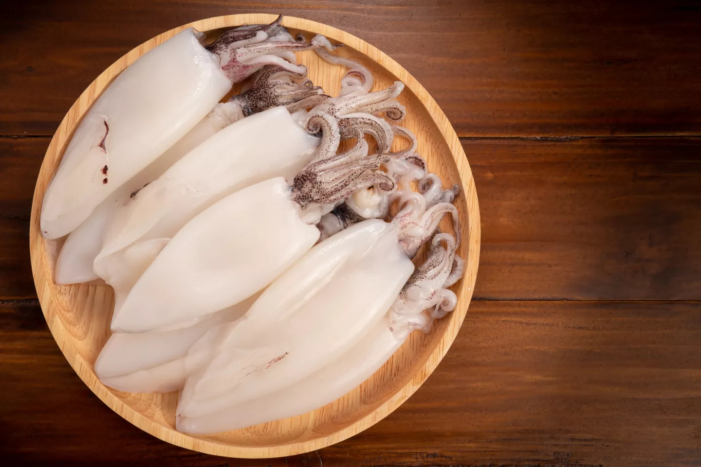 Primer plano de plato de calamares crudo sobre mesa de madera