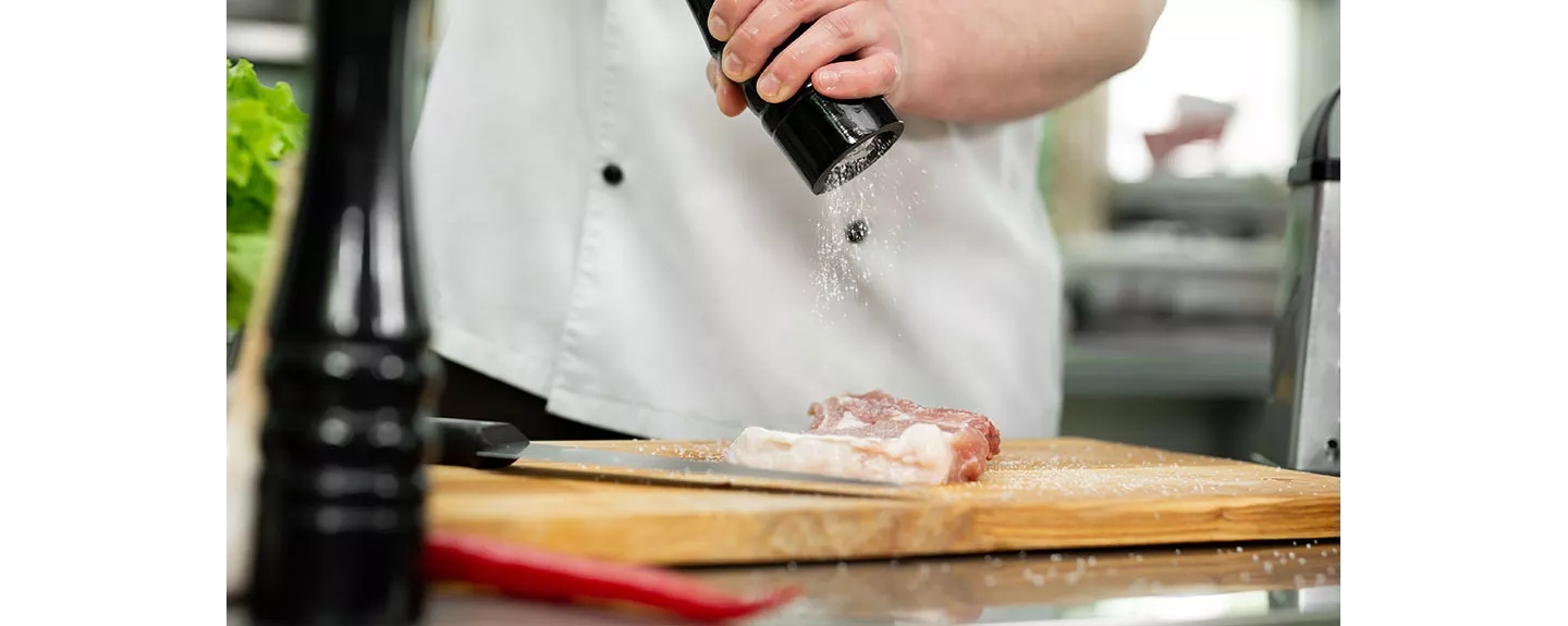 Chef salpimentando carne cruda sobre una tabla de cocina antes de macerar
