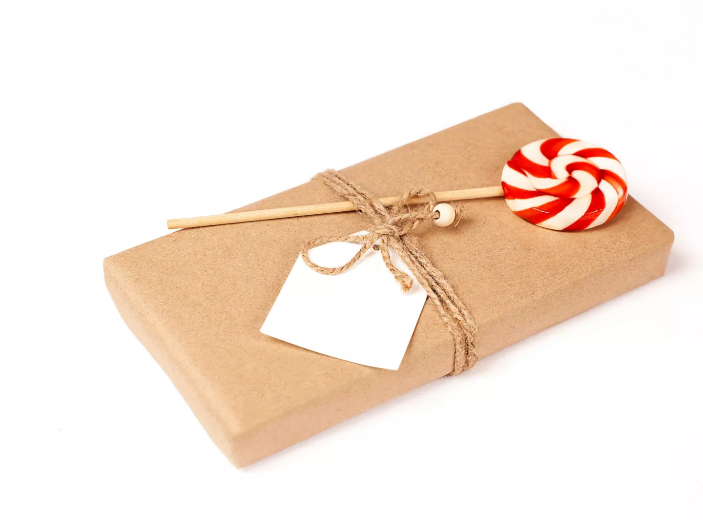 Regalo envuelto en papel kraft con etiqueta blanca, cuerda rústica y piruleta decorativa roja y blanca