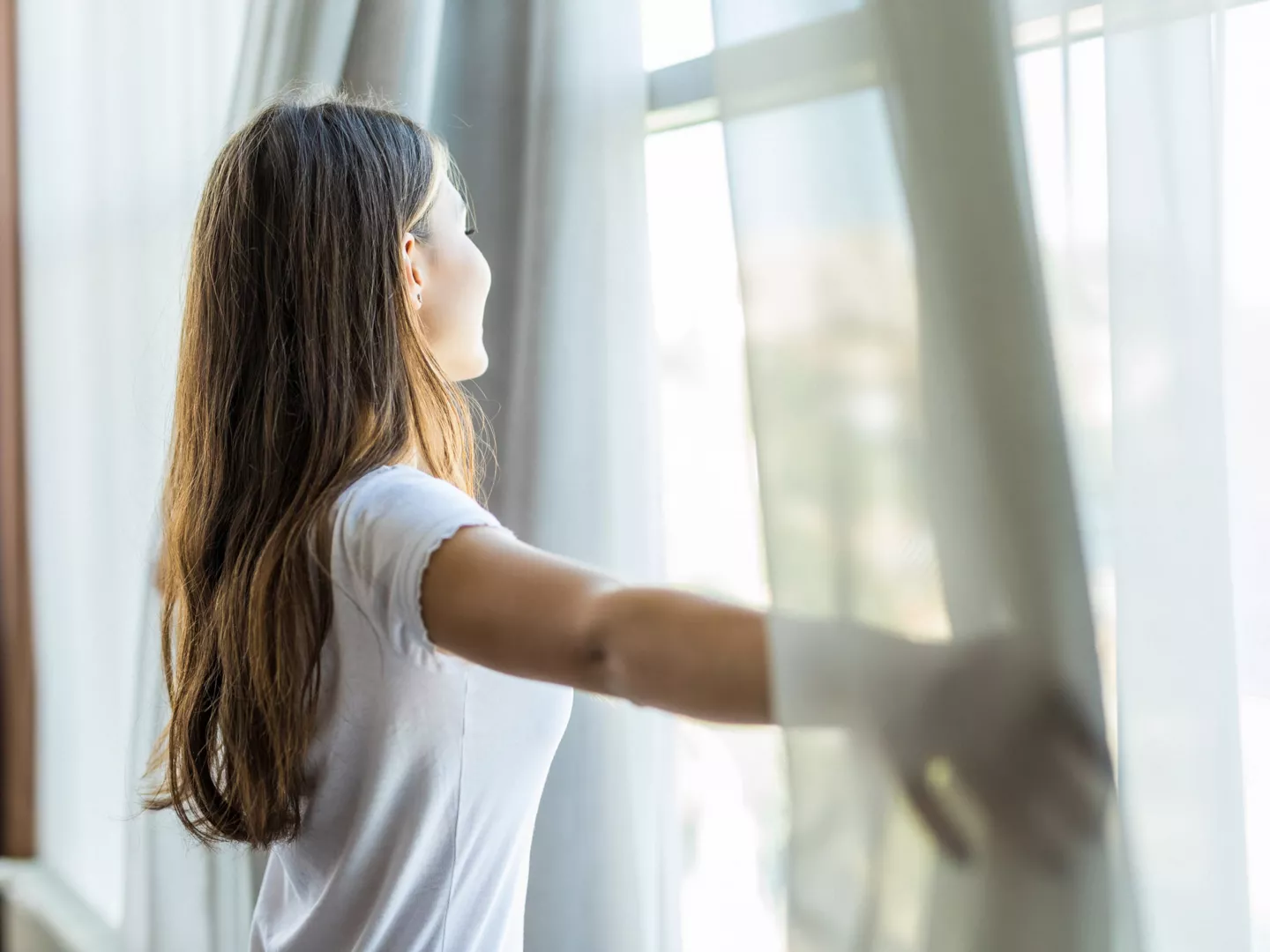 Mujer abriendo cortinas ventilando casa 