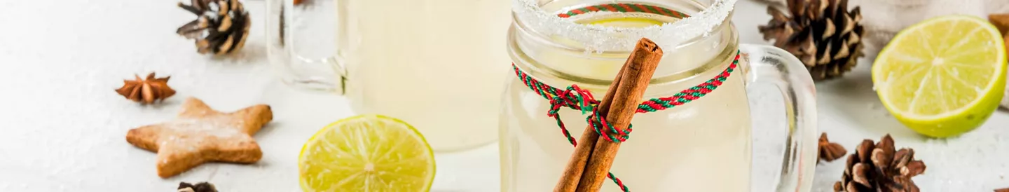 Coctel navideño en tarro decorado con canela, azúcar y lima, junto a galleta de estrella y piñas de Navidad