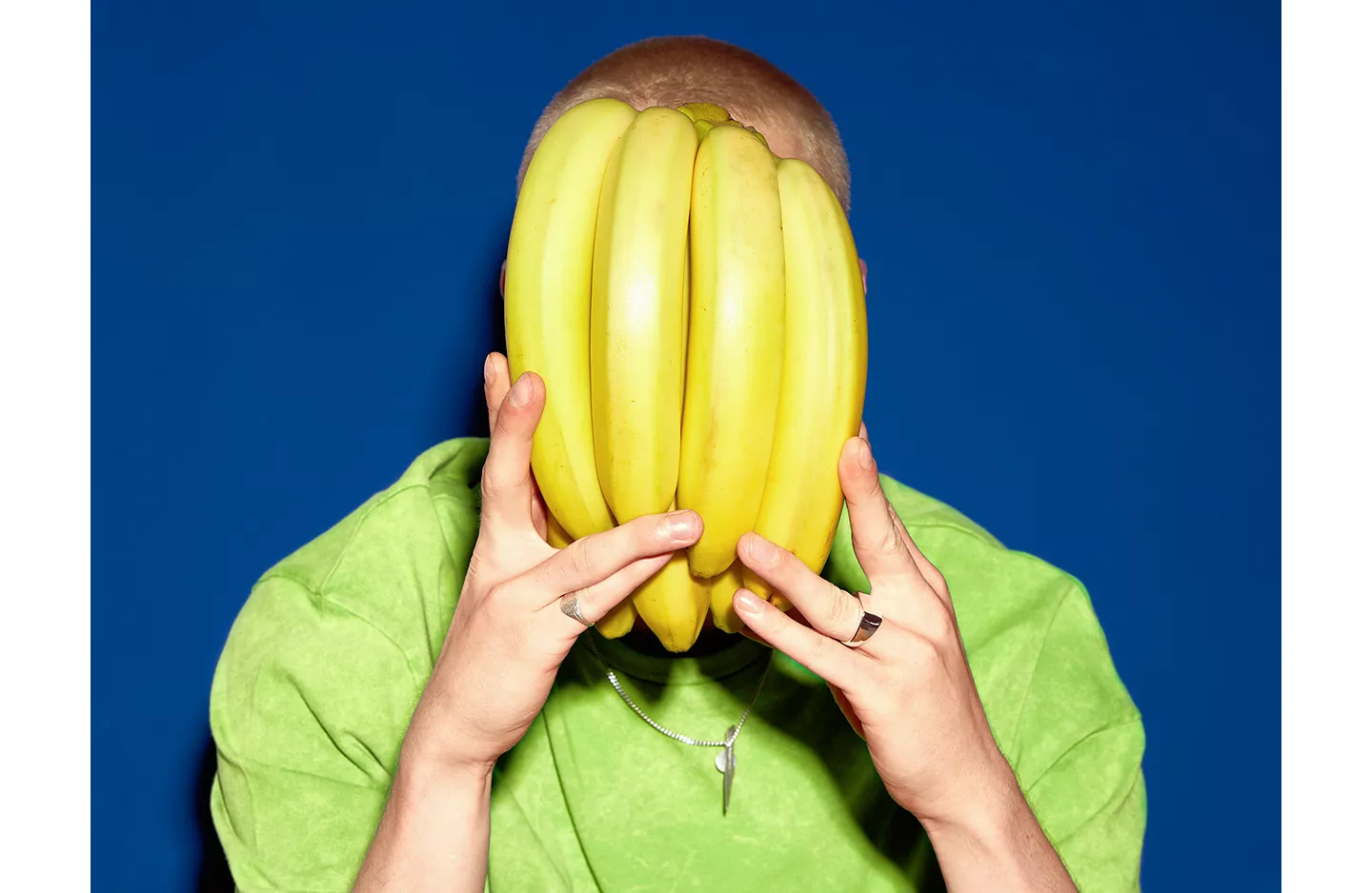 Person hält sich einen Bund Bananen vor ihr Gesicht.
