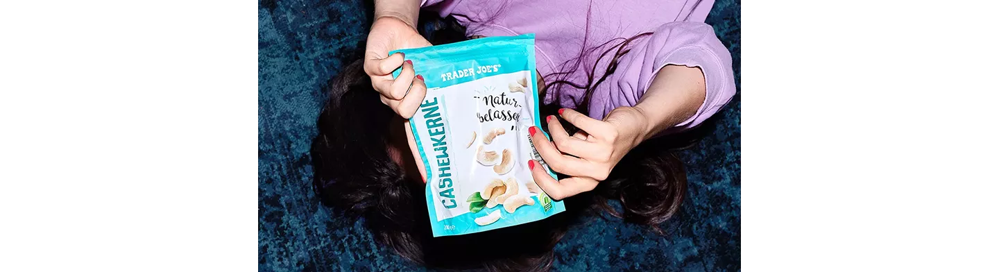 Frau liegt auf dem Boden und hält eine Packung Cashewkerne nach oben in die Kamera.