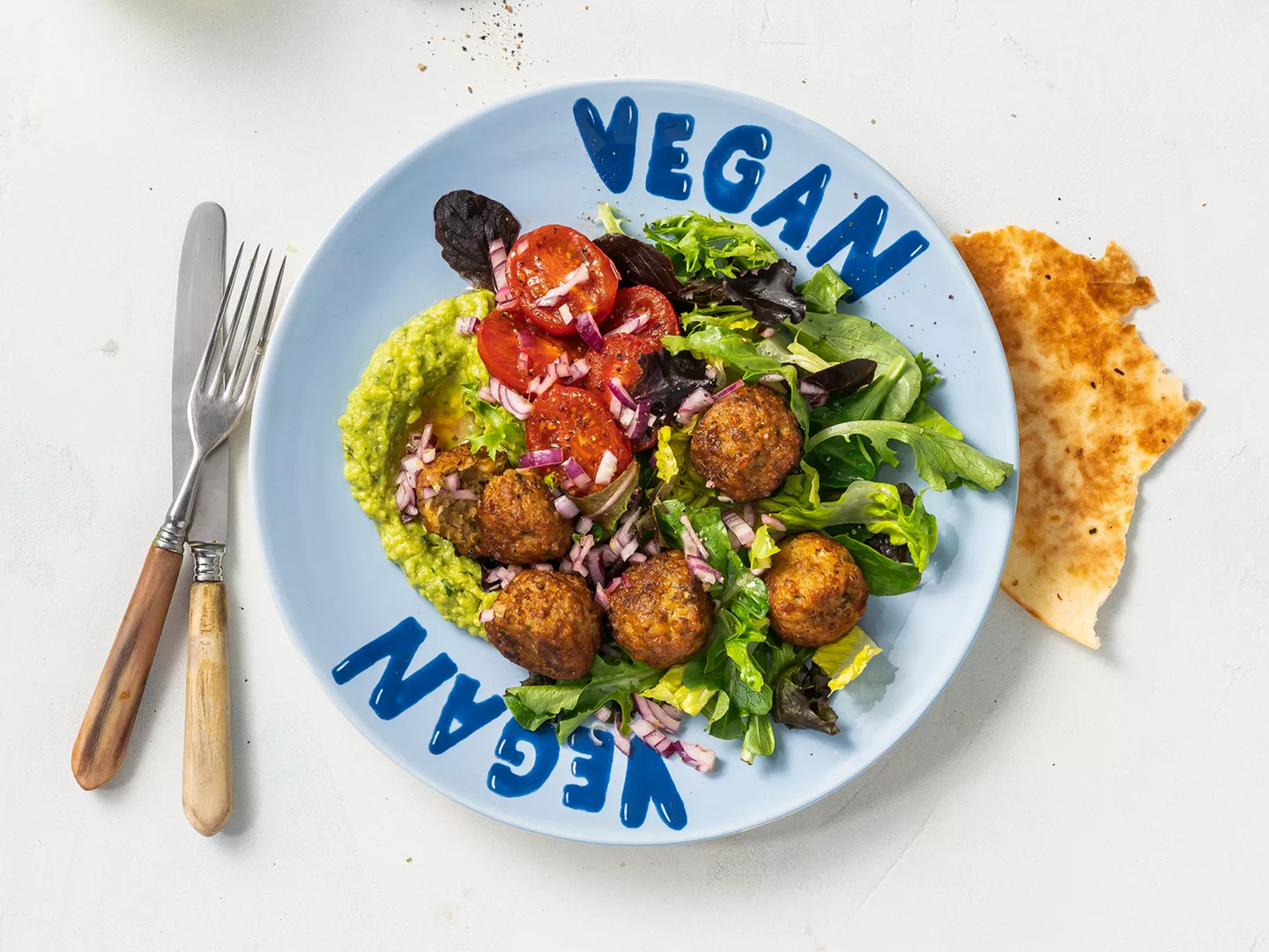 Teller in Blau mit der Aufschrift "vegan" und einem Falafelgericht.