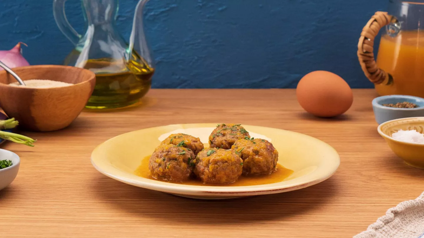 Albóndigas caseras en salsa servidas en plato amarillo con ingredientes frescos de fondo