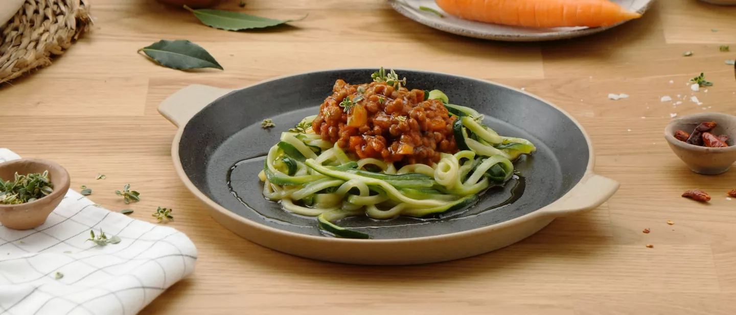 Plato de espaguetis de calabacín con ragú de lentejas, servido en una sartén de cerámica.