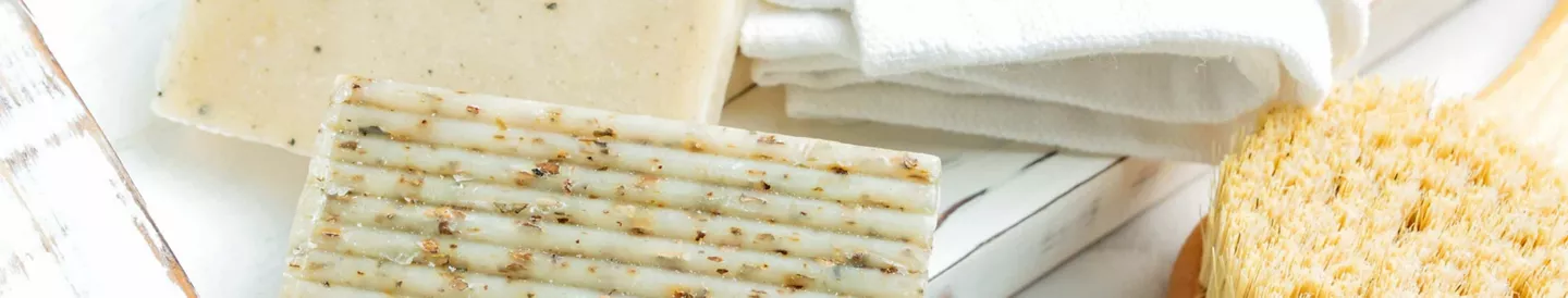 Pastilla de jabón casero con aceite usado y hierbas naturales, sobre fondo de toalla y esponja
