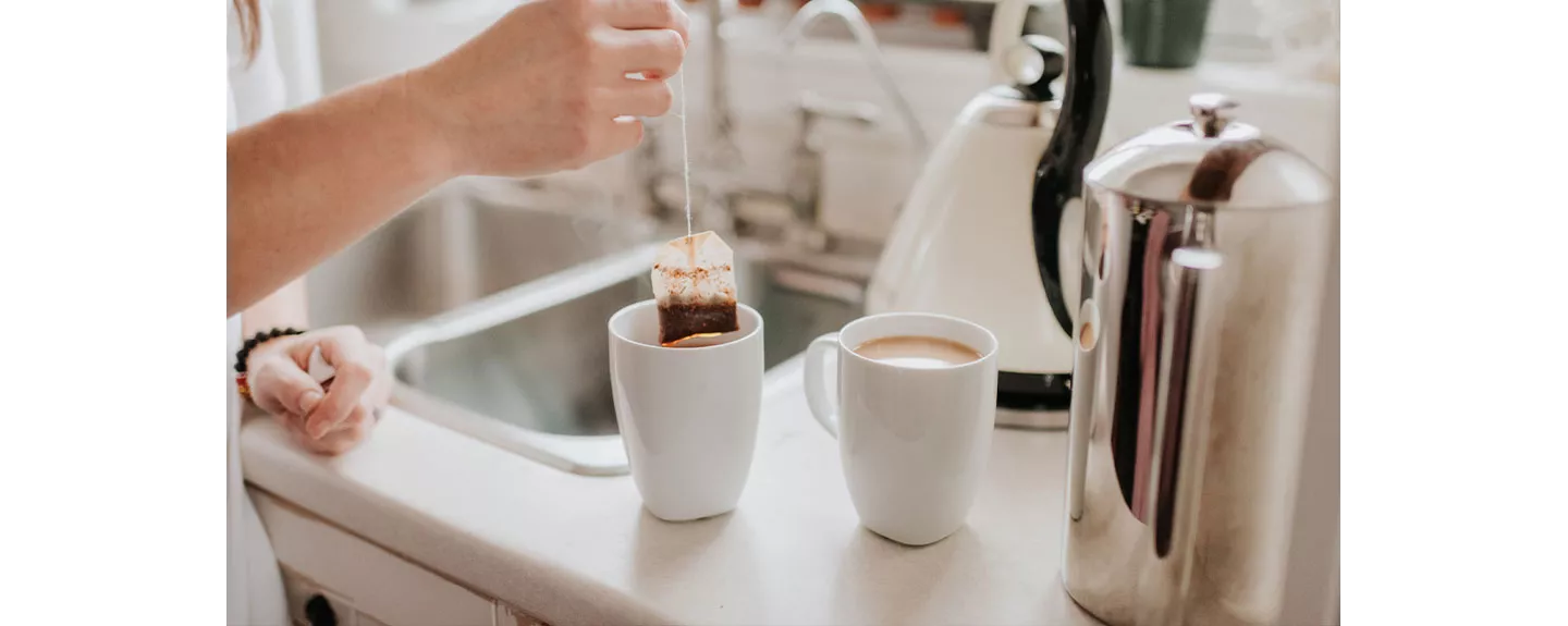 Una persona sacando una bolsa de té de una taza, al lado de otra taza de café
