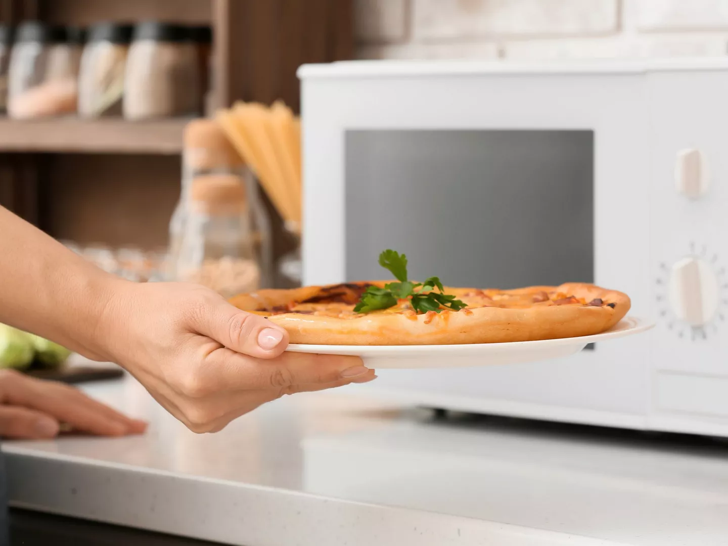 Persona sacando una pizza casera del microondas sobre un plato blanco, lista para servir