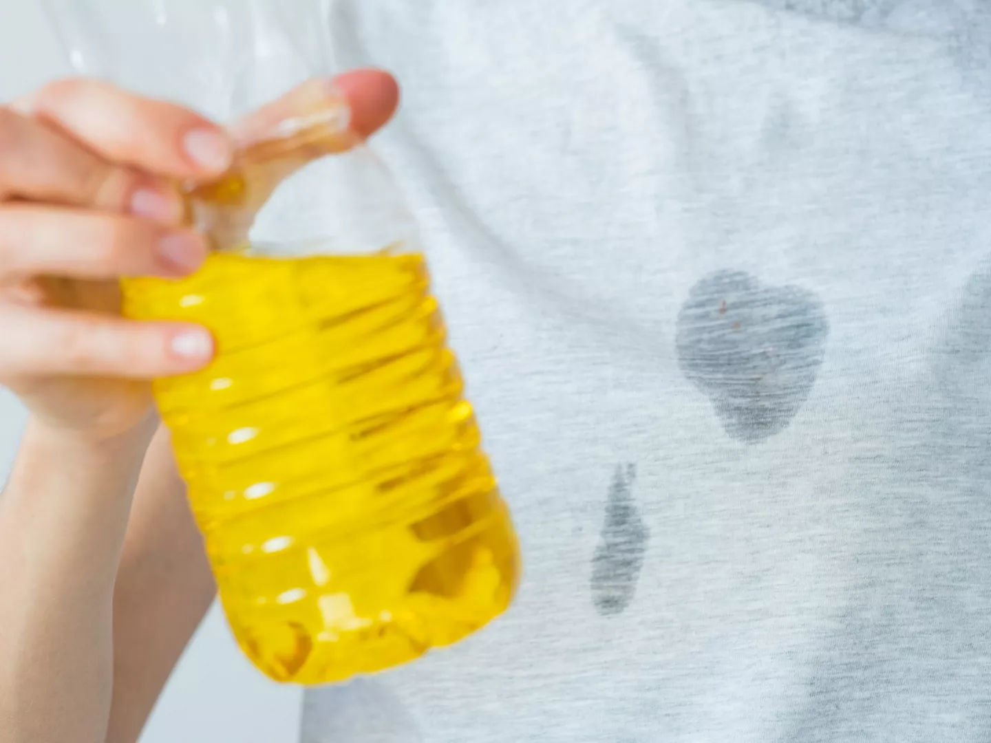 Persona sosteniendo botella aceite camiseta manchada