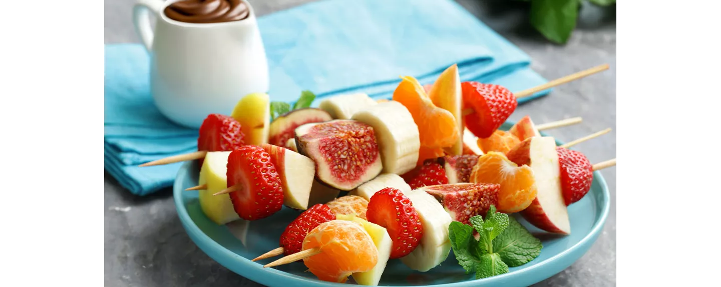 Brochetas de fruta fresca con fresas, plátano, mandarina e higos, acompañadas de chocolate, una merienda saludable y divertida para compartir.