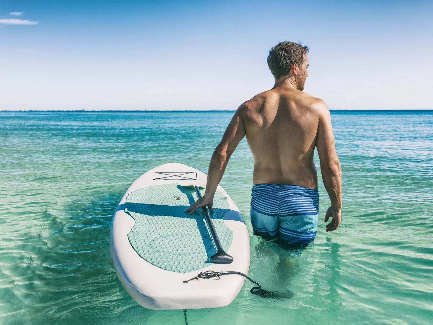 Hombre entrando al agua con tabla de paddle surf hinchable