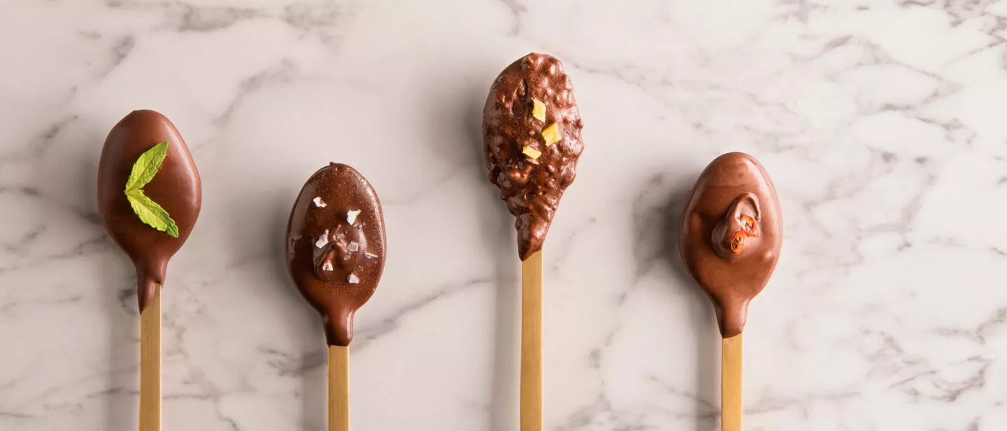 Cucharillas cubiertas de chocolate casero con diferentes toppings, una idea creativa y sencilla para quienes quieren hacer chocolate casero de forma original.