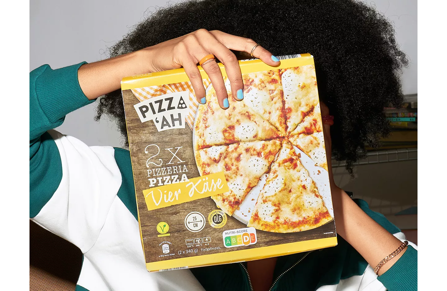 Person hält sich eine TK-Pizza vors Gesicht.