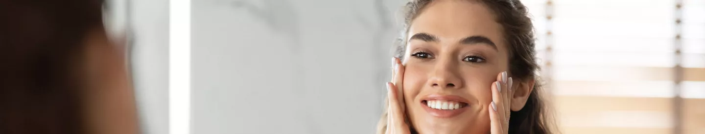 Mujer sonriendo manos rostro frente espejo cuarto baño