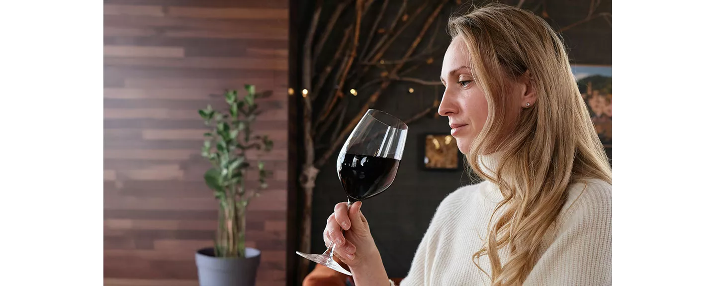 Mujer sosteniendo una copa de vino tinto, evaluando su aroma y cuerpo