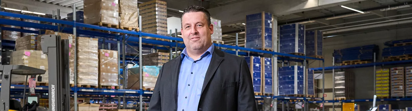 Führungskraft in der Logistik steht in einem modernen Lager von ALDI Nord vor Hochregalen mit Warenpaletten.