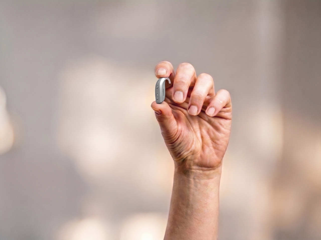 Hand holding small silver hearing aid