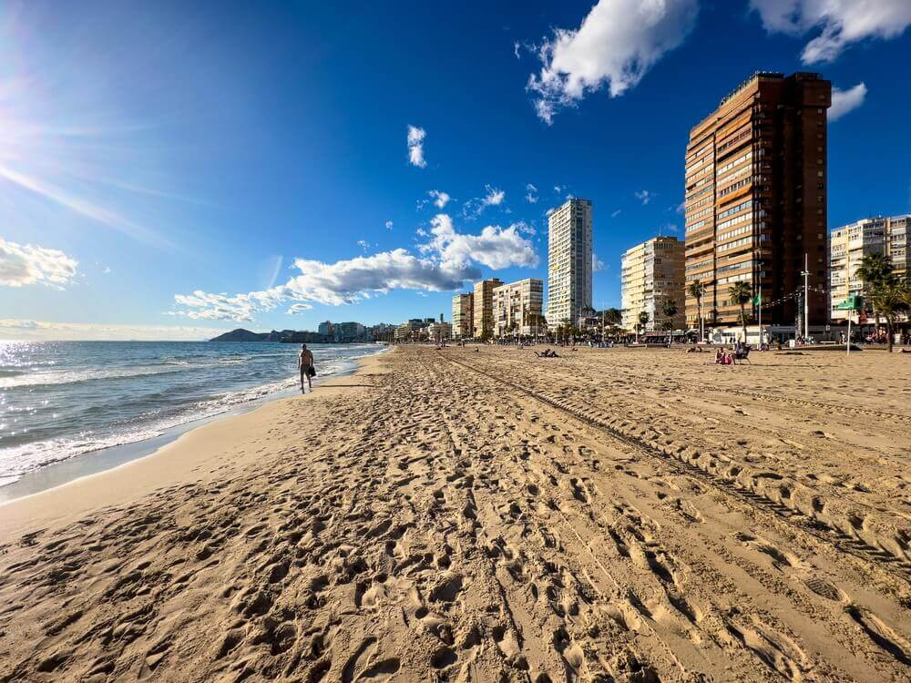 Levante Beach: City beach with white sand and a man walking 