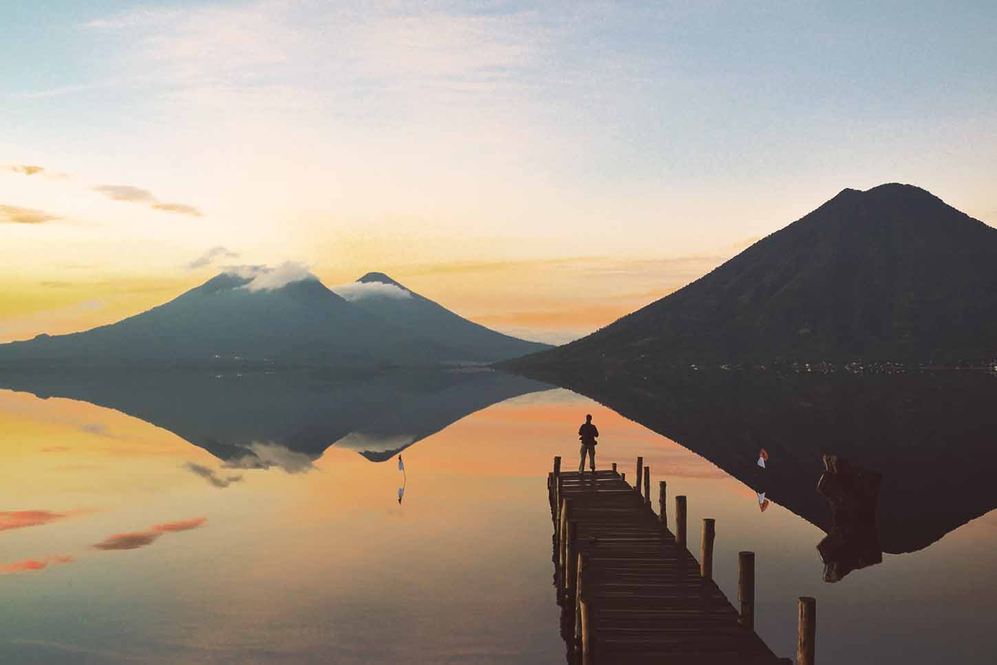 Guatemala: Man rowing on a lake at sundown with volcano backdrop