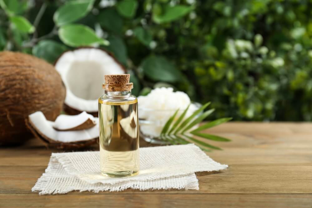 Coconut Oil: A glass bottle of oil and open coconuts on a table