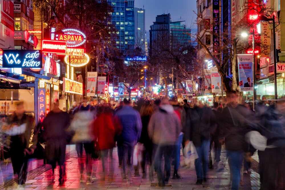Kızılay Square: A blurred crowd of people walking down a central street lit by shop signs