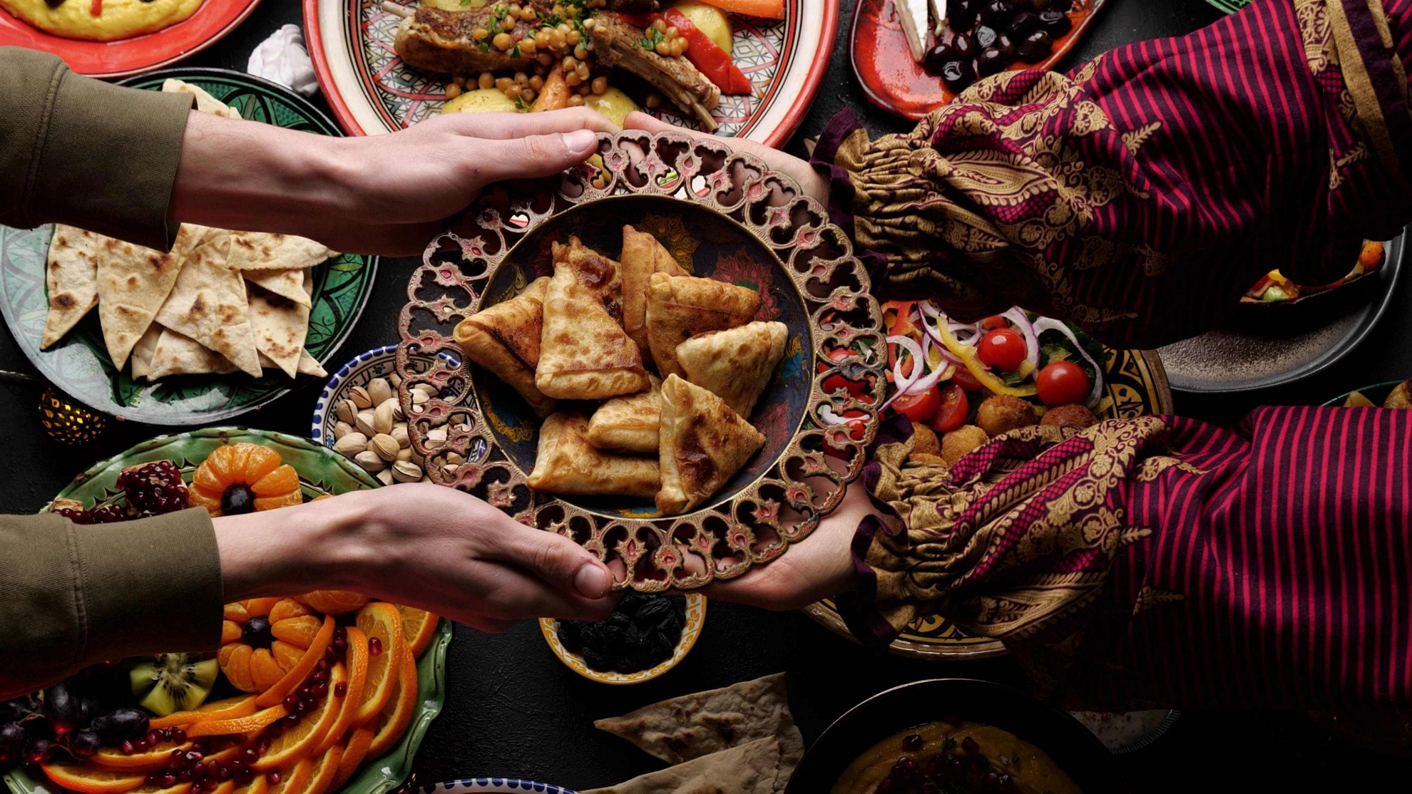 Arabische Küche: vier Hände halten eine Schale über einem Tisch mit vielen Speisen.
