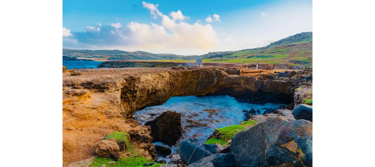This rock bridge surrounded by rugged terrain and greenery is a perfect example of Aruba nature.