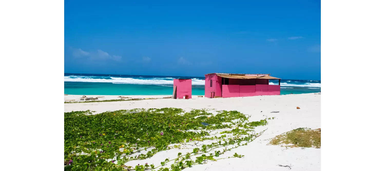 White sand dunes in Aruba surround a small pink hut on Boca Prins Beach.
