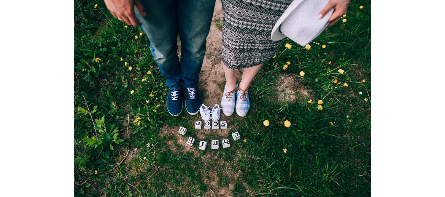 Babymoon: Füße von werdenden Eltern mit Babyschühchen und "coming soon"