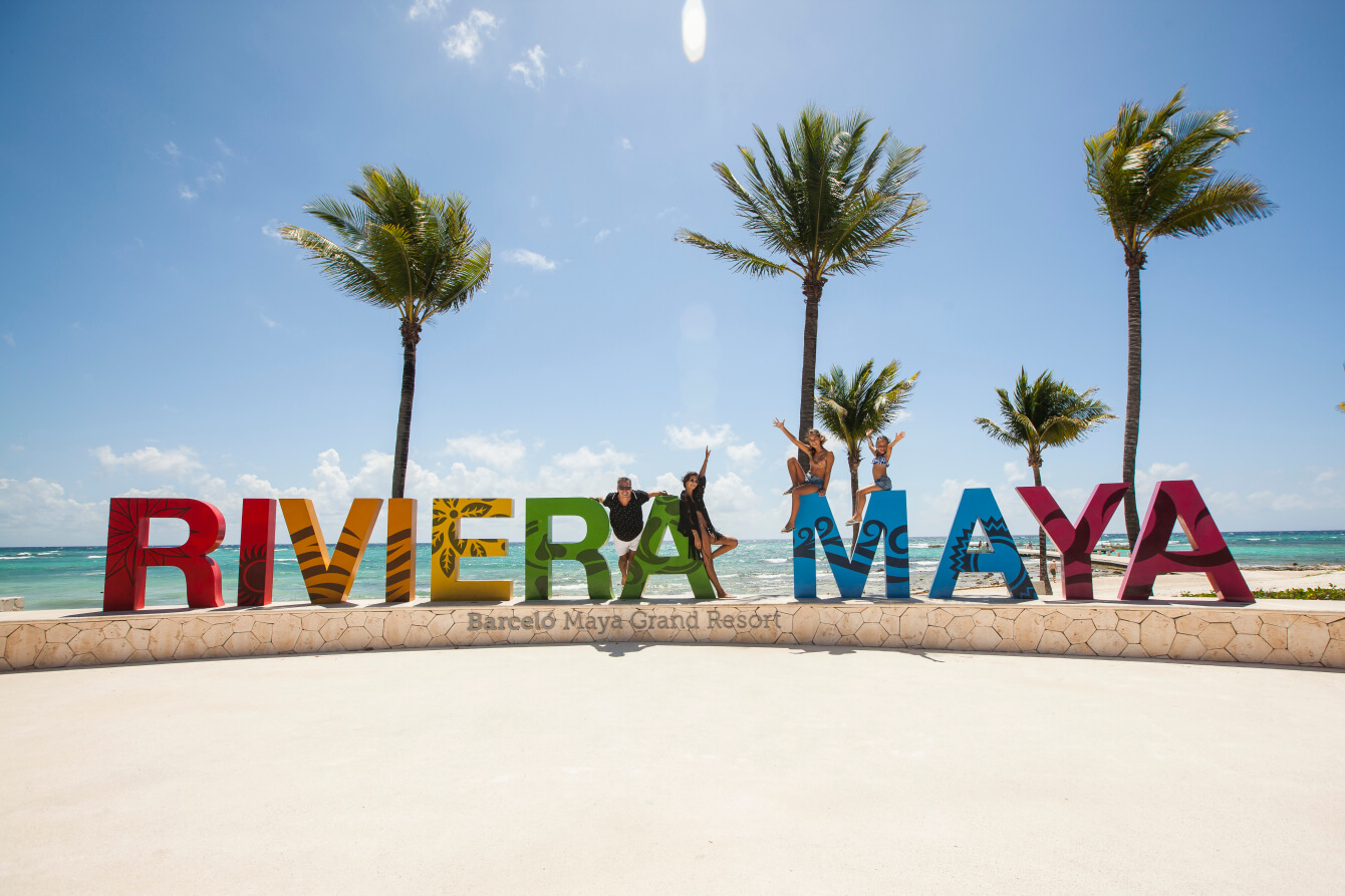 A family of four poses at the colorful Riviera Maya sign at Barceló Maya Grand Resort.