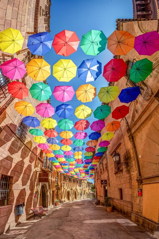 Bunte Schirme zwischen Häuserfassaden im Poble espanyol in Barcelona.