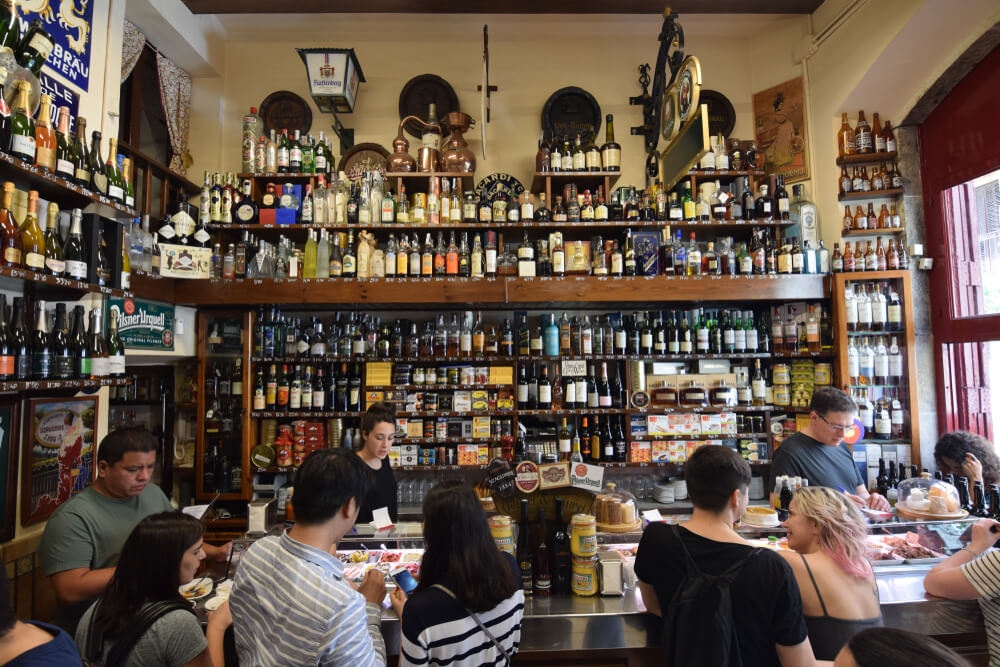 Poble Sec: An old tapas bar full of people with a wall of bottles behind the bar