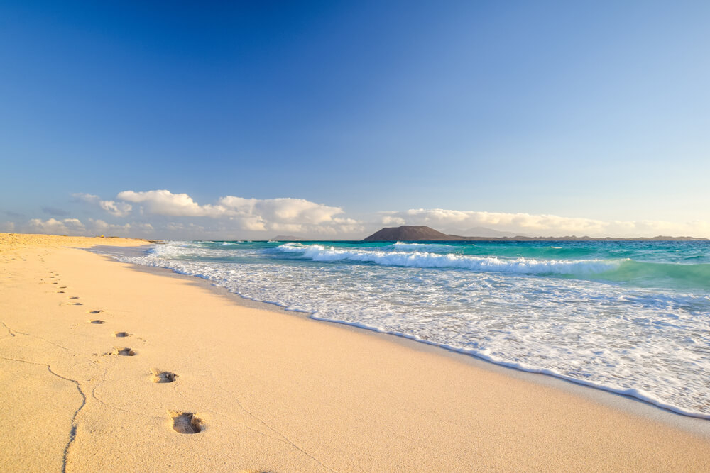 Best beaches in Fuerteventura: Golden sand and blue sea of Corralejo with volcano in the distance