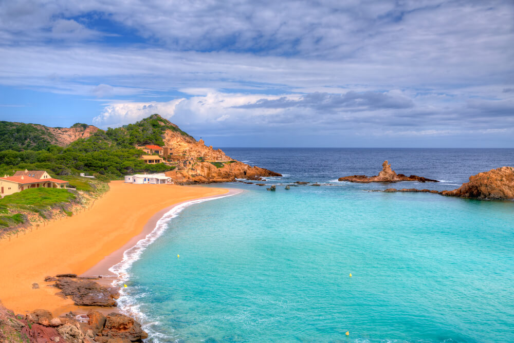 Best beaches in Menorca: View of Cala Pregonda with the rocks and boats in the distance