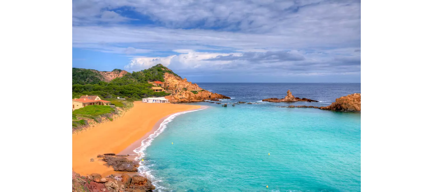 Best beaches in Menorca: View of Cala Pregonda with the rocks and boats in the distance