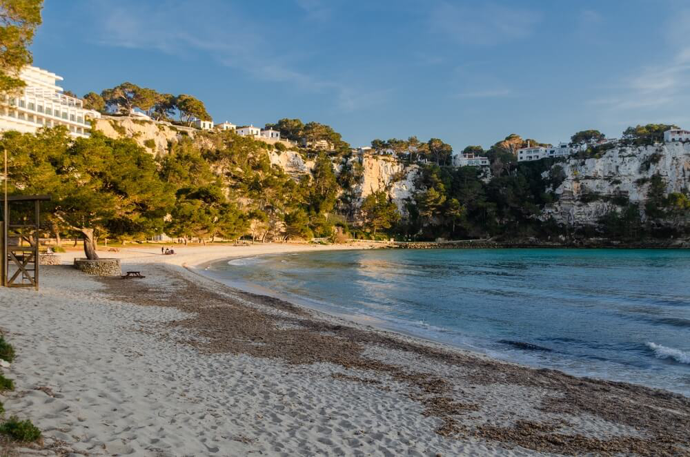 Best coves in Menorca: White sand of Cala Galdana with white buildings in the background