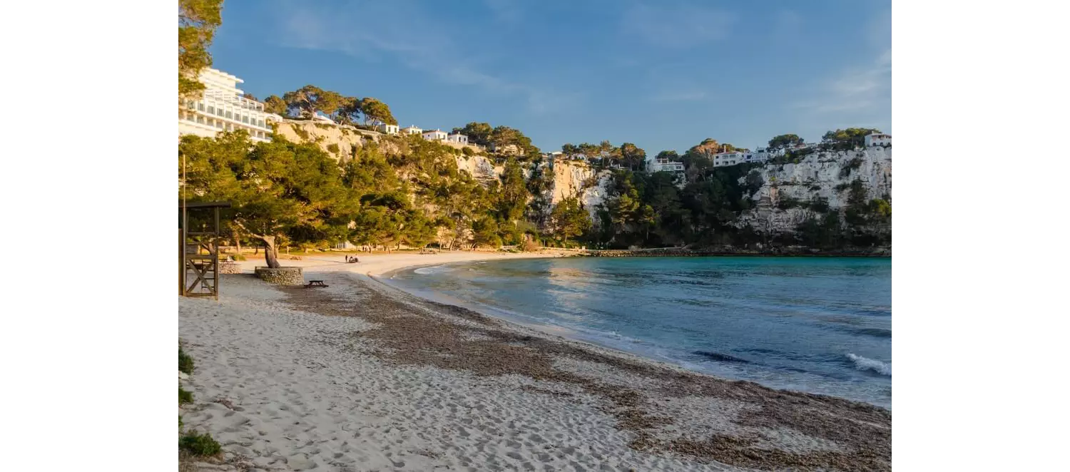 Best coves in Menorca: White sand of Cala Galdana with white buildings in the background