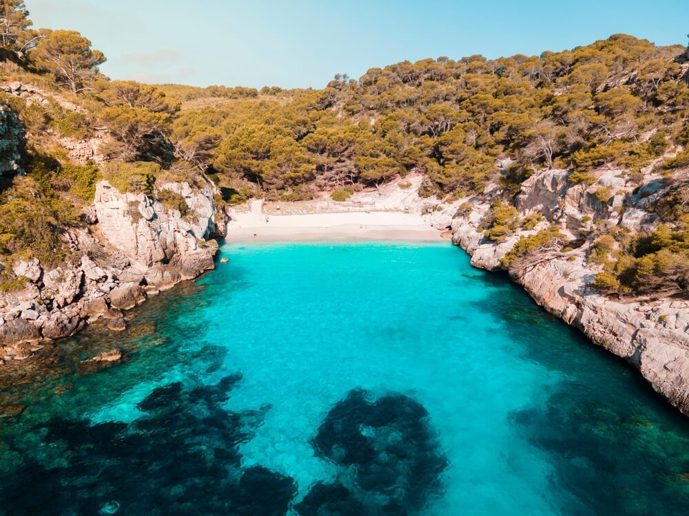 Secluded beaches Menorca: Aerial view of Cala Mitjana surrounded by greenery